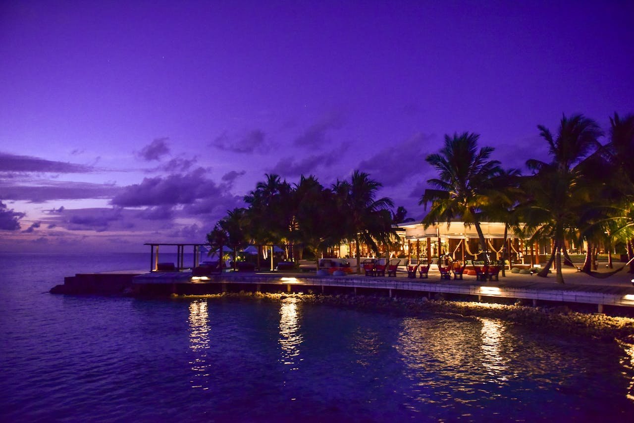 A breathtaking view of a tropical resort at twilight, surrounded by palm trees and reflecting on the ocean.